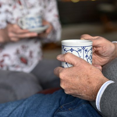 Sicht auf die Hände zweier älterer Menschen die eine Kaffeetasse halten und sich gegenübersitzen